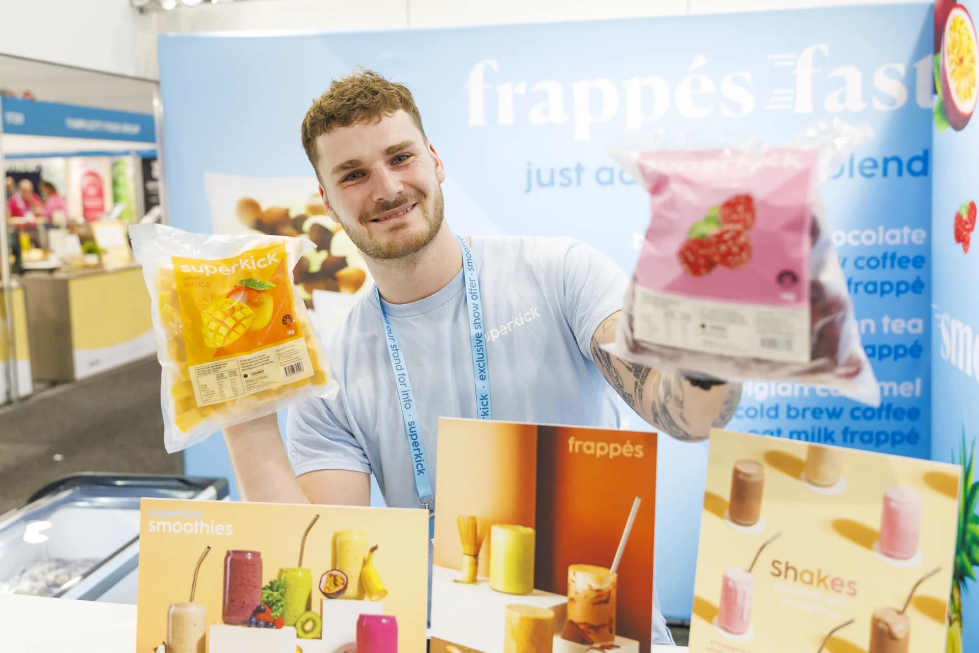An exhibitor holding up packs of frozen fruit at a frappé and smoothie stand