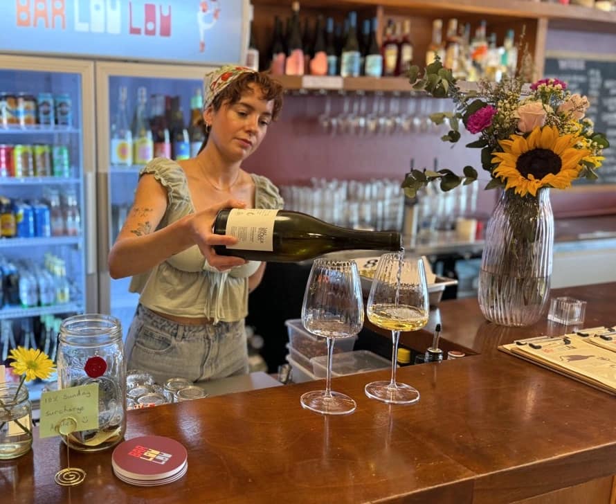 Louise Marks pouring wine into a glass behind the Bar Lou Lou counter