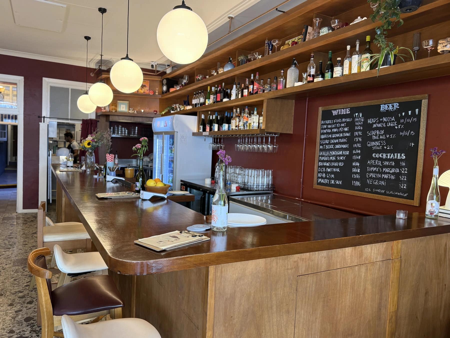 The timber bar, burgundy walls and pendant lights at Bar Lou Lou