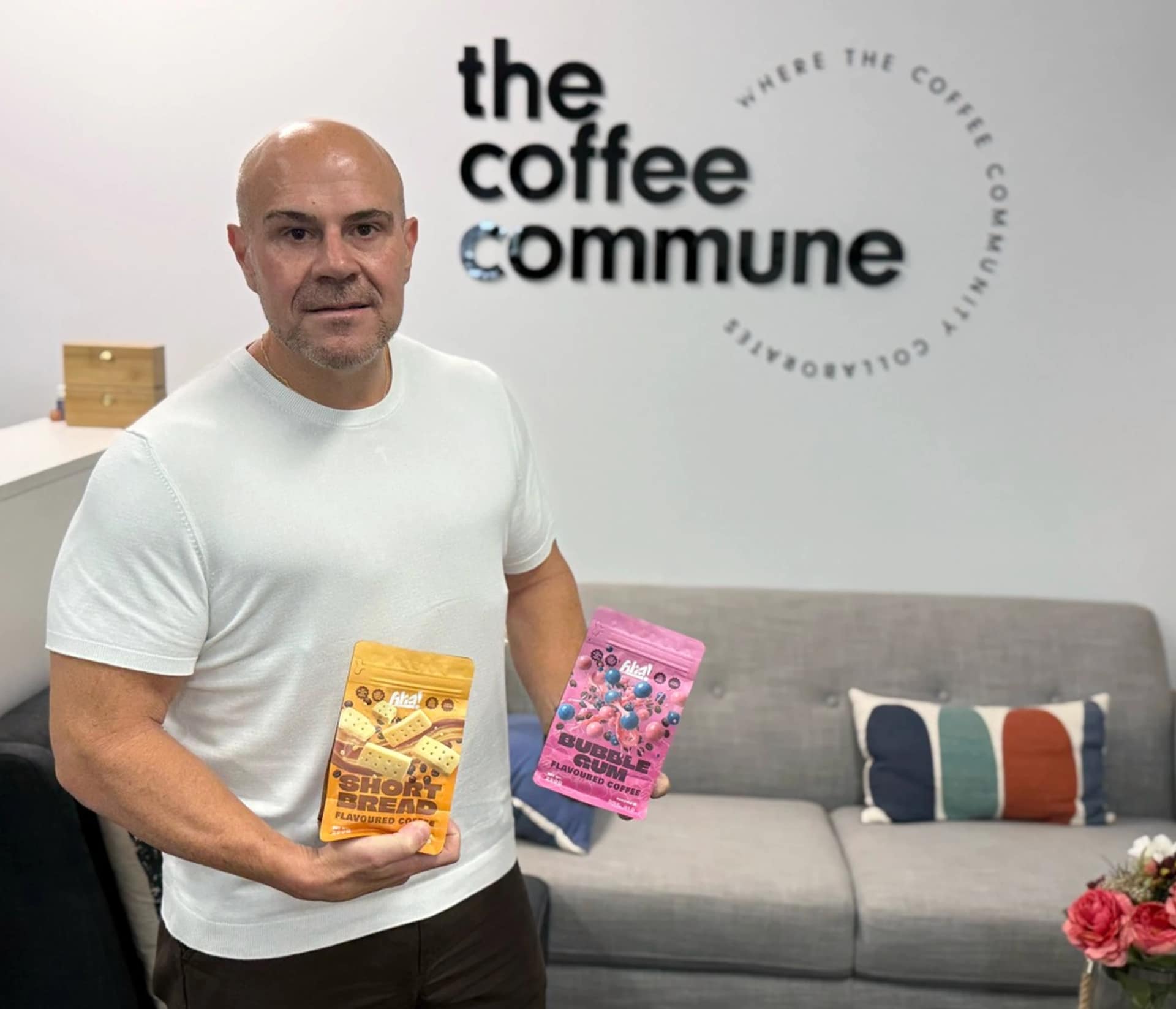 Phillip Di Bella holding coffee products beneath The Coffee Commune sign