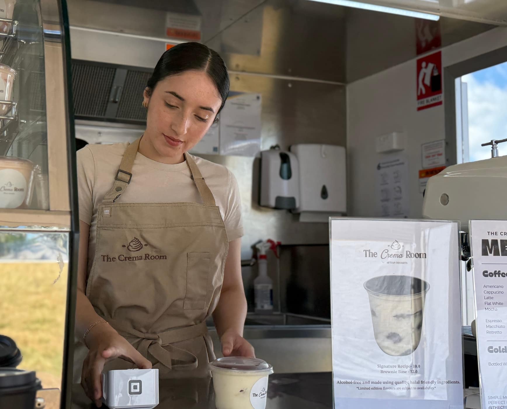 Suzan preparing an order at The Crema Room counter beside the tiramisu display