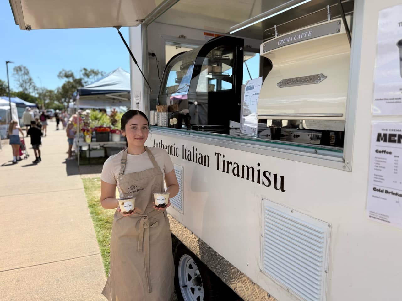 Suzan holding two tiramisu cups beside The Crema Room trailer at a market