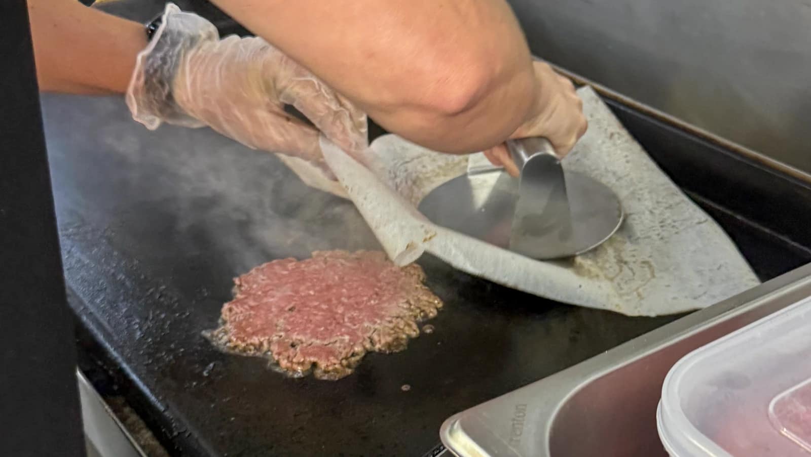 Burger patties being cooked on the truck’s hotplate beside a burger press.