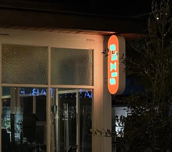 The Sixes sign glowing beside At Sixes and Sevens' white timber windows at night