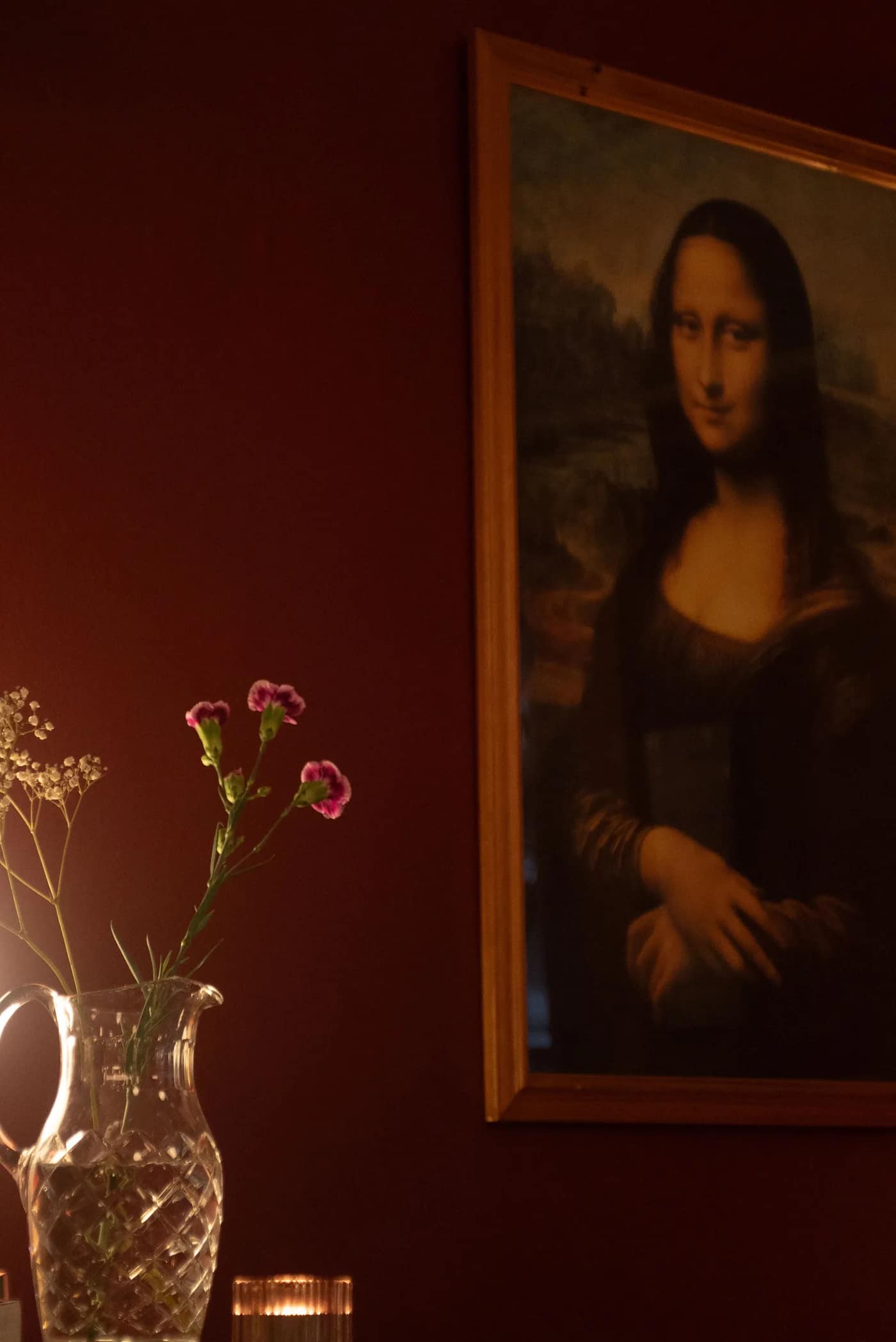 A burgundy corner at Bar Lou Lou with a framed Mona Lisa print and fresh flowers