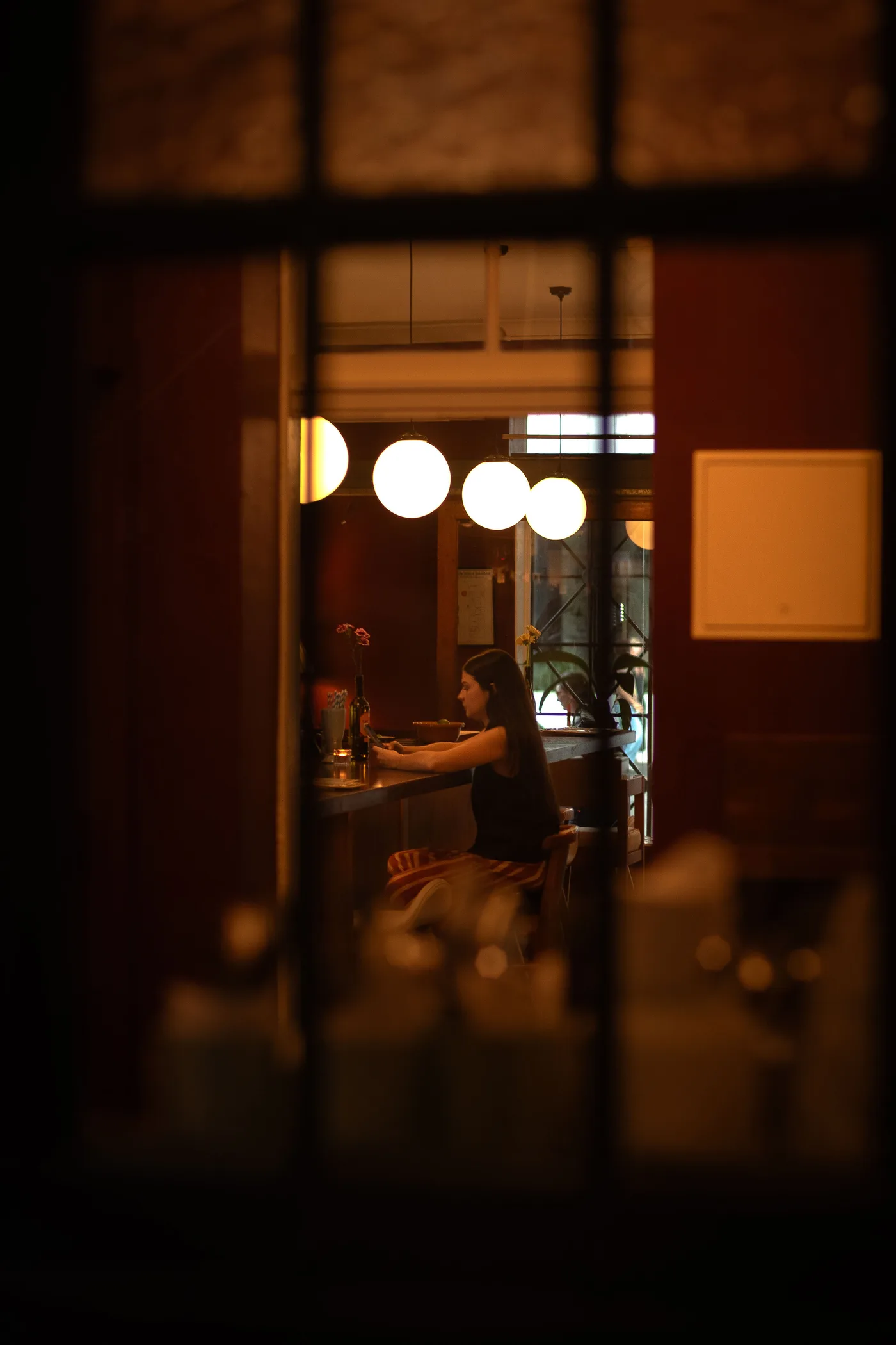 Bar Lou Lou glowing at night, seen through a window on Barry Parade