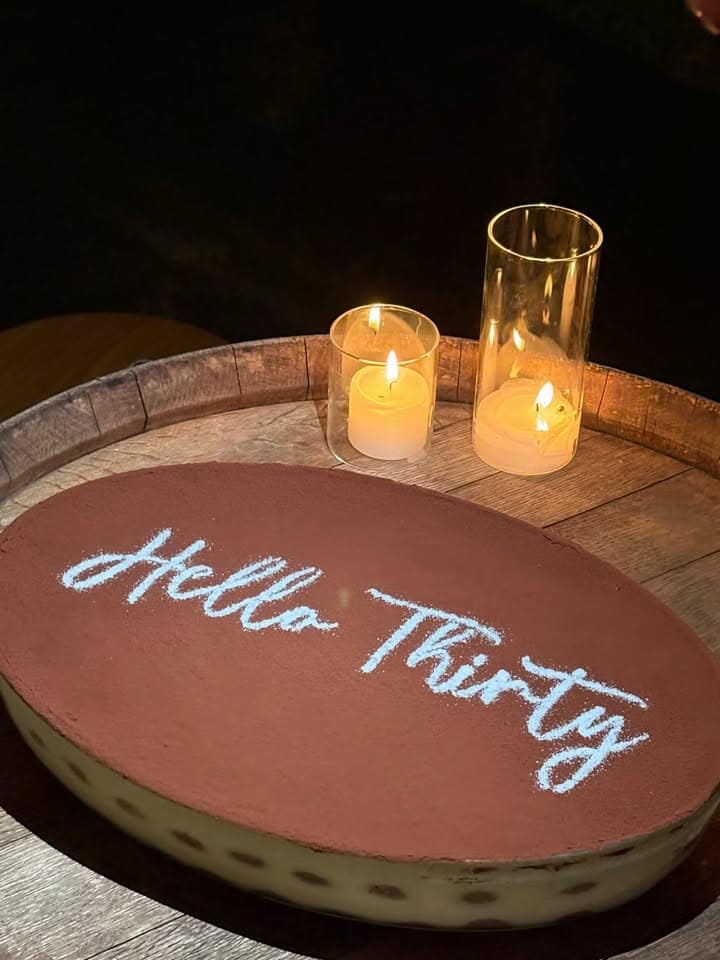 A tiramisu dusted with "Hella Thirty" beside candles for a birthday