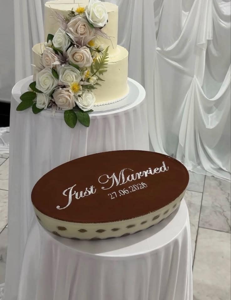 An oval tiramisu dusted with "Just Married" beside a wedding cake