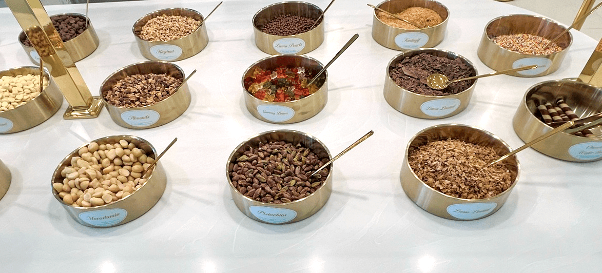 Rows of gold-coloured topping bowls on a white counter at Luma Newstead