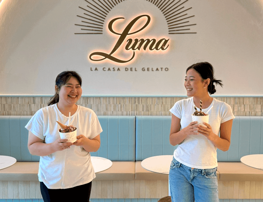 Two Luma team members laughing with gelato cups beneath the illuminated Luma sign
