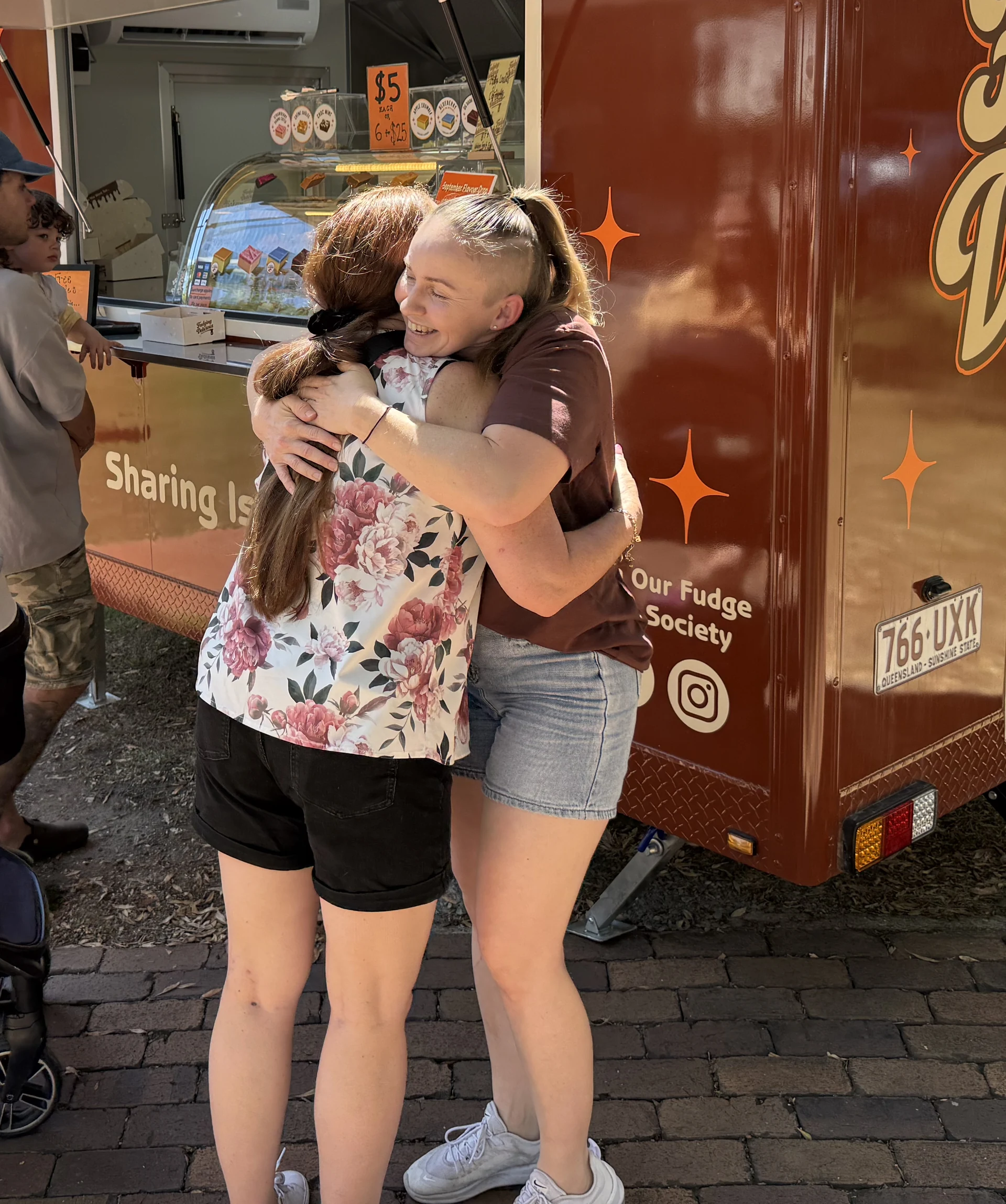 Sarah smiling as she hugs a customer beside the fudge trailer
