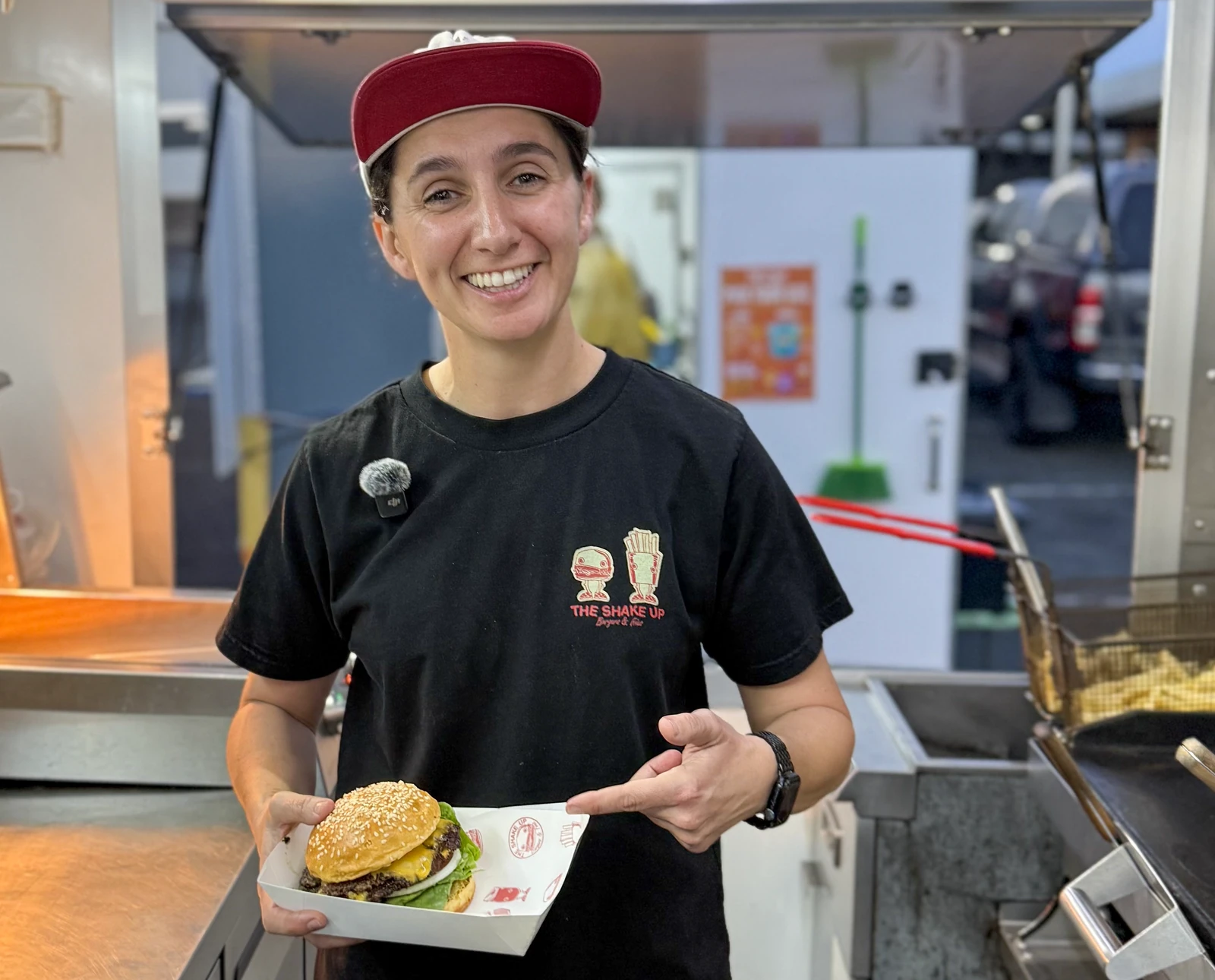 Atiana smiling and pointing towards the burger she is holding inside The Shake Up truck