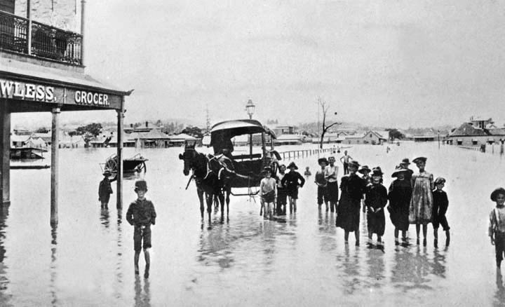 People and a horse-drawn vehicle standing in floodwater on James Street in 1893