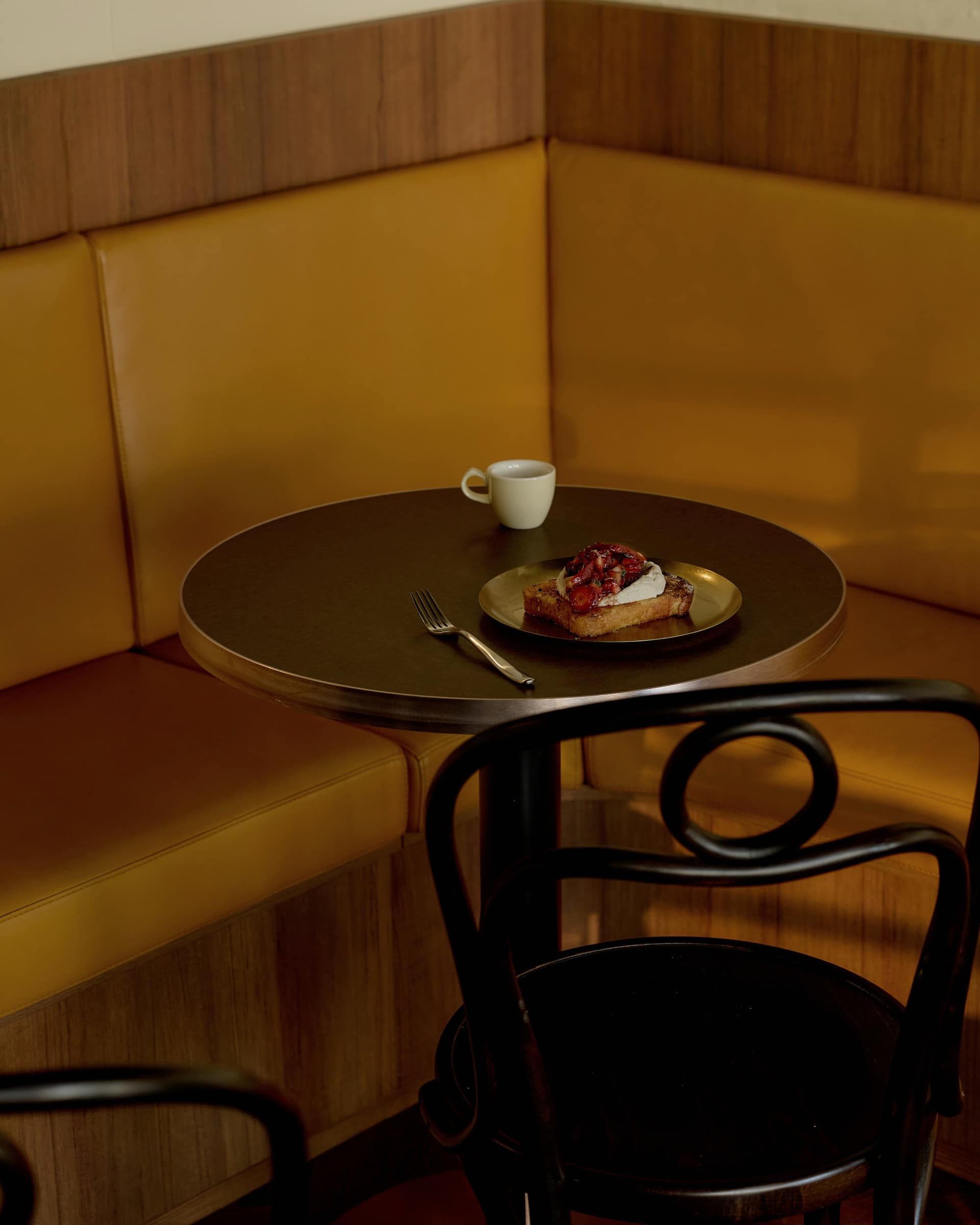 Brioche with strawberries and a coffee on a round table beside the golden booth at Bistro Tino
