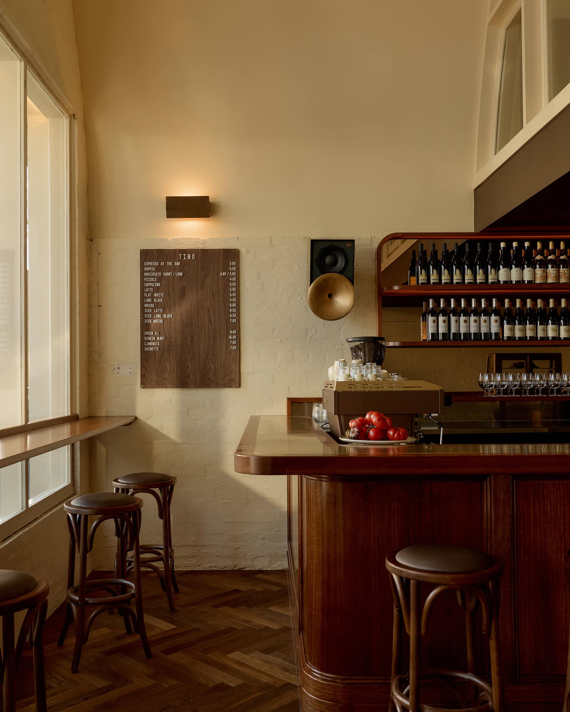 Daylight across Bistro Tino's curved timber bar, window stools and cream walls