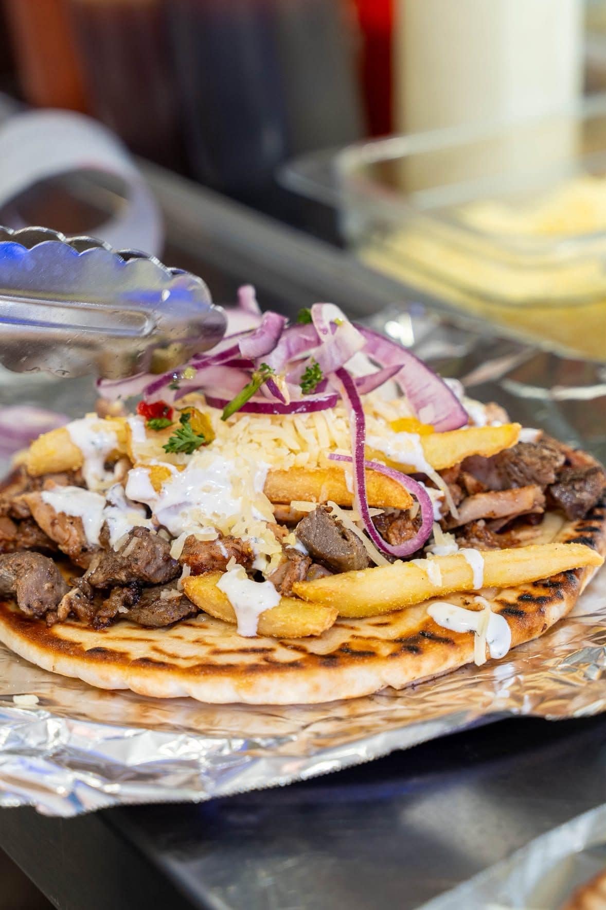 An open yiros with meat, chips, onion and sauce at Ozi Yiros